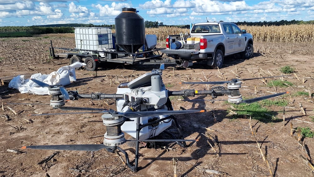 DJI Agras T100 auf einem Stoppelfeld, dahinter Anhänger und Pickup für die Versorgung